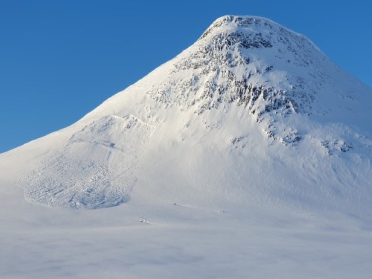 Fotograf: Lavinprognoser.se Ett snöklätt fjäll med blå himmel bakom.